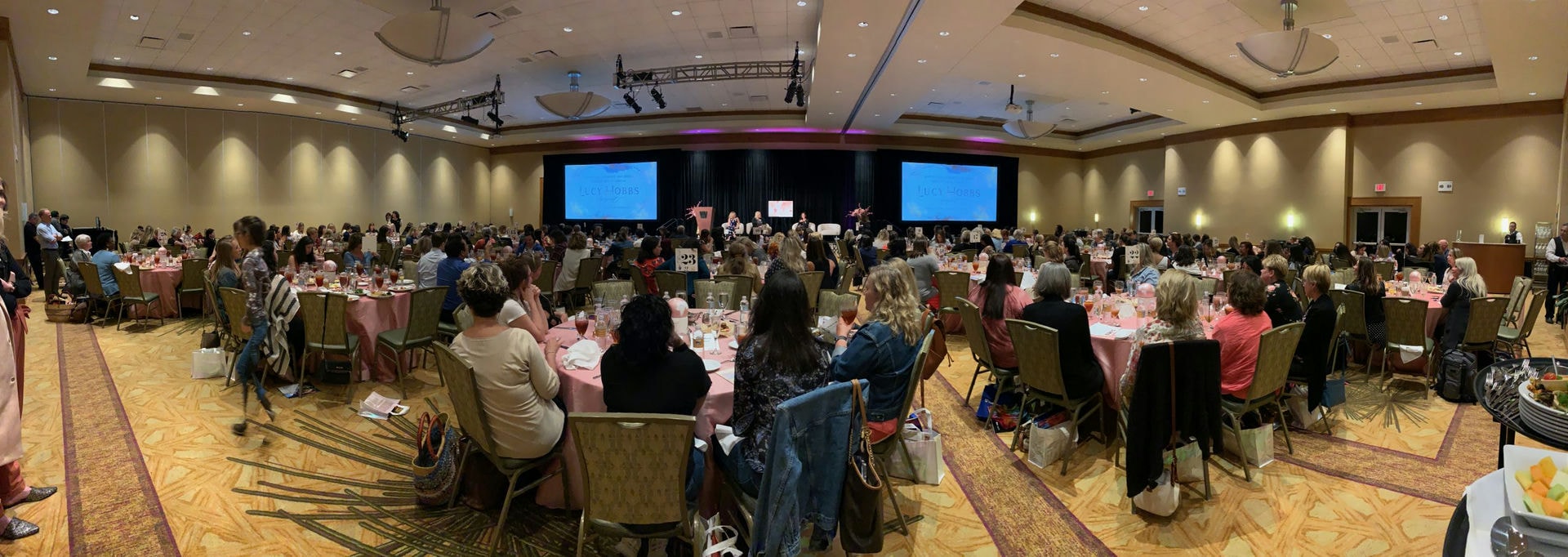 Attendees seated around circular tables at a banquet, watching a presentation.