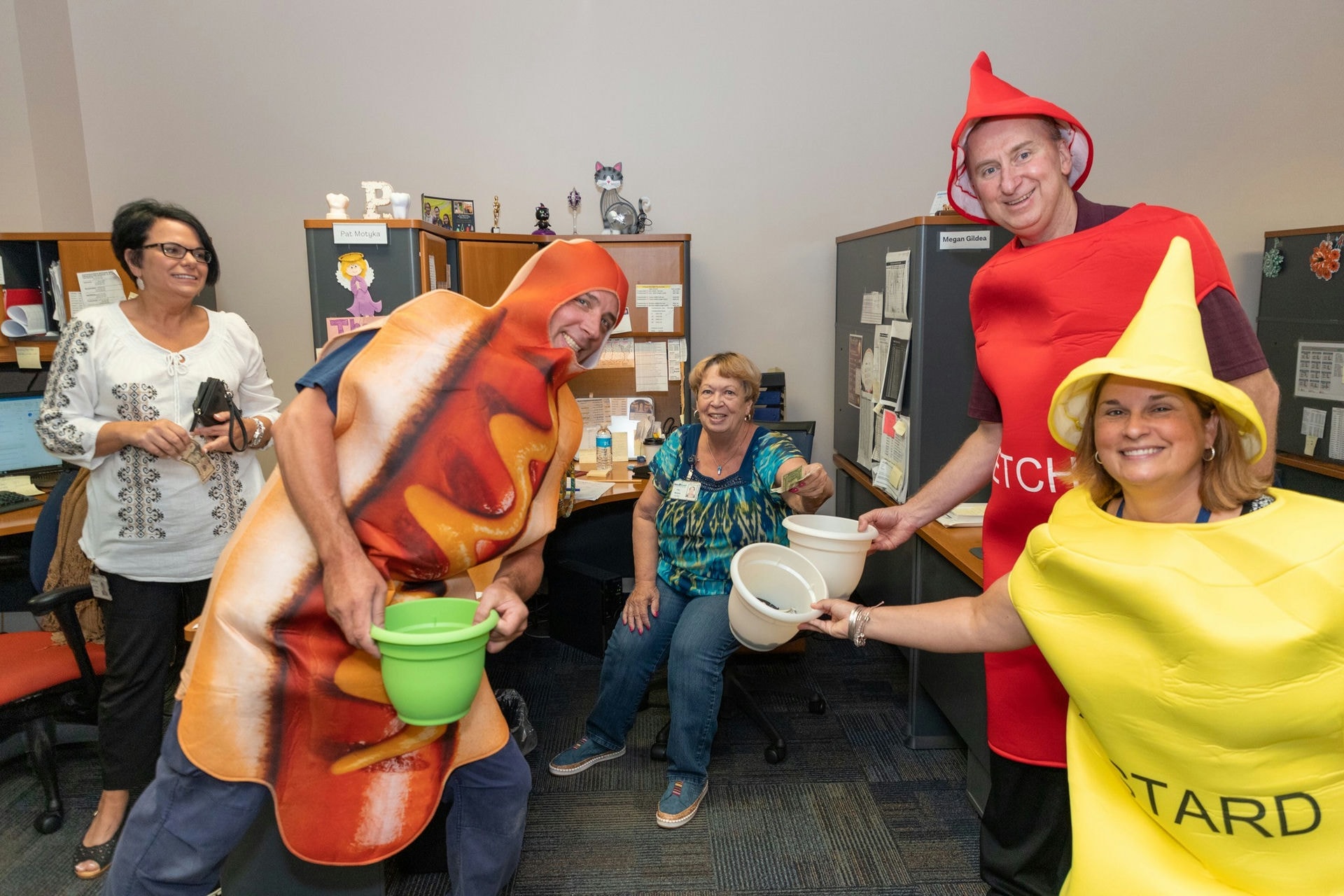 The Operations Trio in hot dog and condiment costumes collects donations from associates in the Tooth Room.