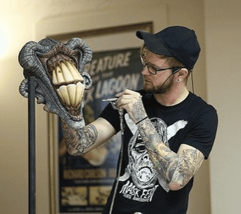 Artist Jordan Patton is shown applying airbrush paint to an oversized model of alien teeth.