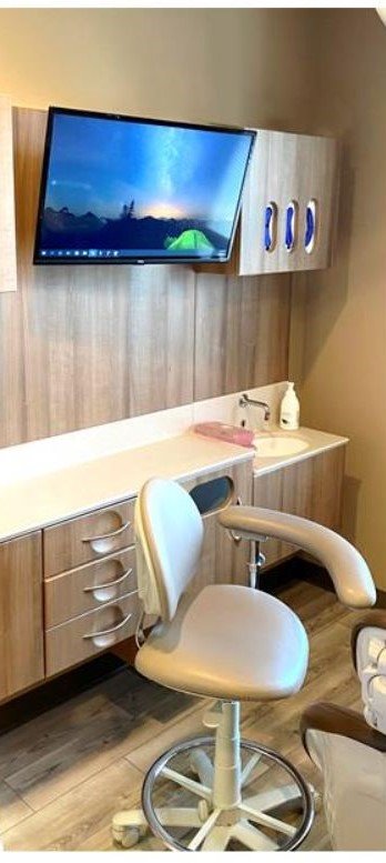 The side workstation in a dental office, including a dentist's chair with an armrest, a large computer monitor screen, and a small sink.
