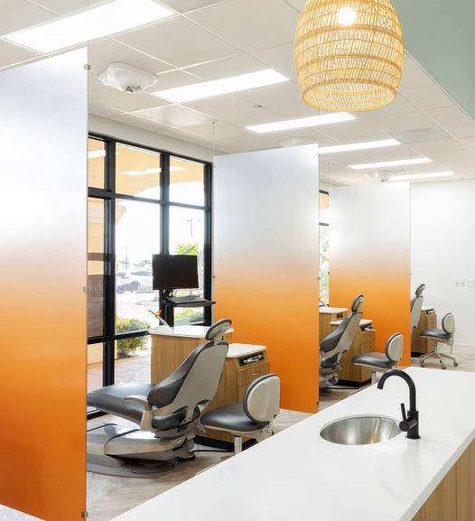 A well-lit dental office decorated with warm neutral tones fading into bright oranges.