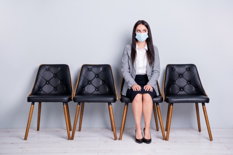 Woman in a suit awaiting a job interview and wearing a medical mask.