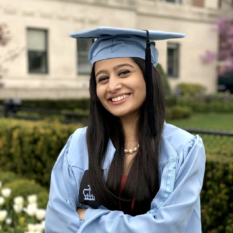 Shreya Sood stands smiling with her arms folded in a graduation cap and gown.