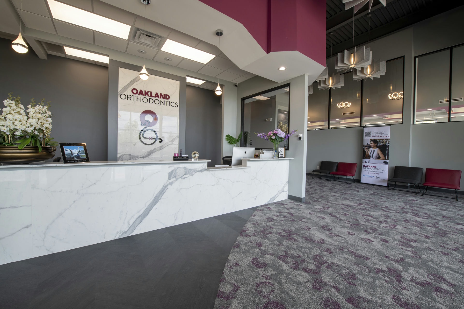 The large, open lobby of Oakland Orthodontics features chandelier light fixtures and a modern gray and marble color scheme.