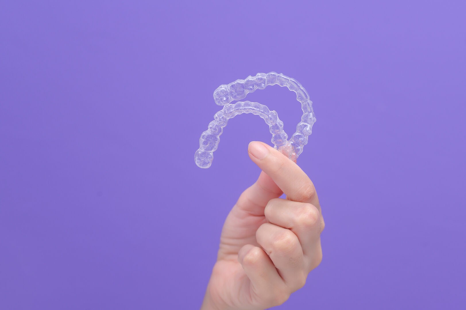 A hand holds two clear aligners up against a blue backdrop.
