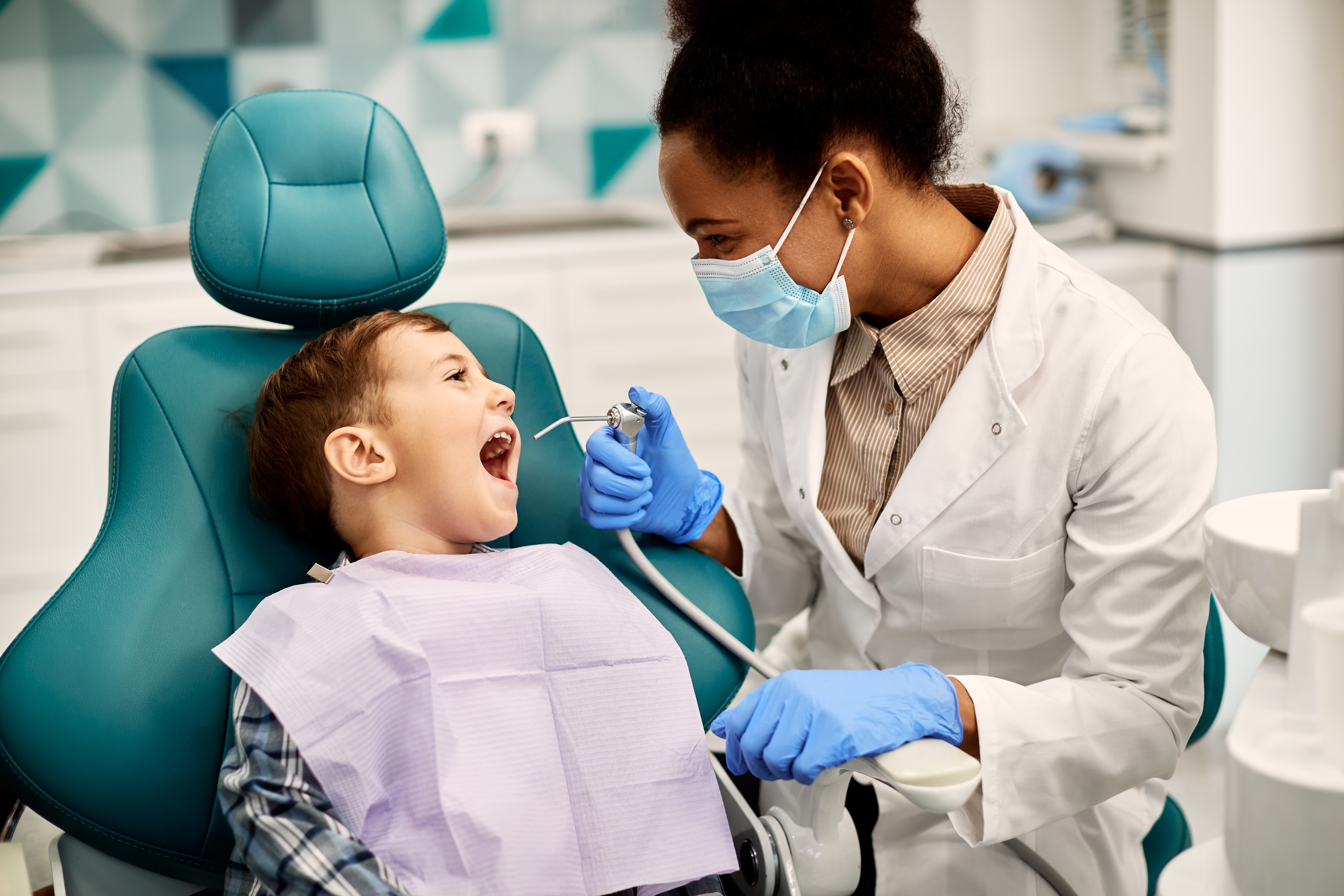 A small boy smiles happily at his dentist who is holding a water spray tool.