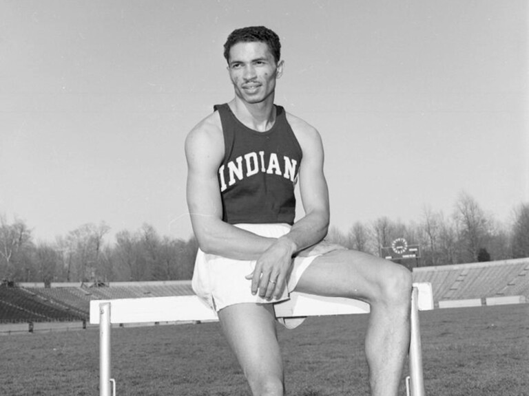 A black and white photo of 1956 Olympic gold medalist Greg Bell sitting on a hurdle.