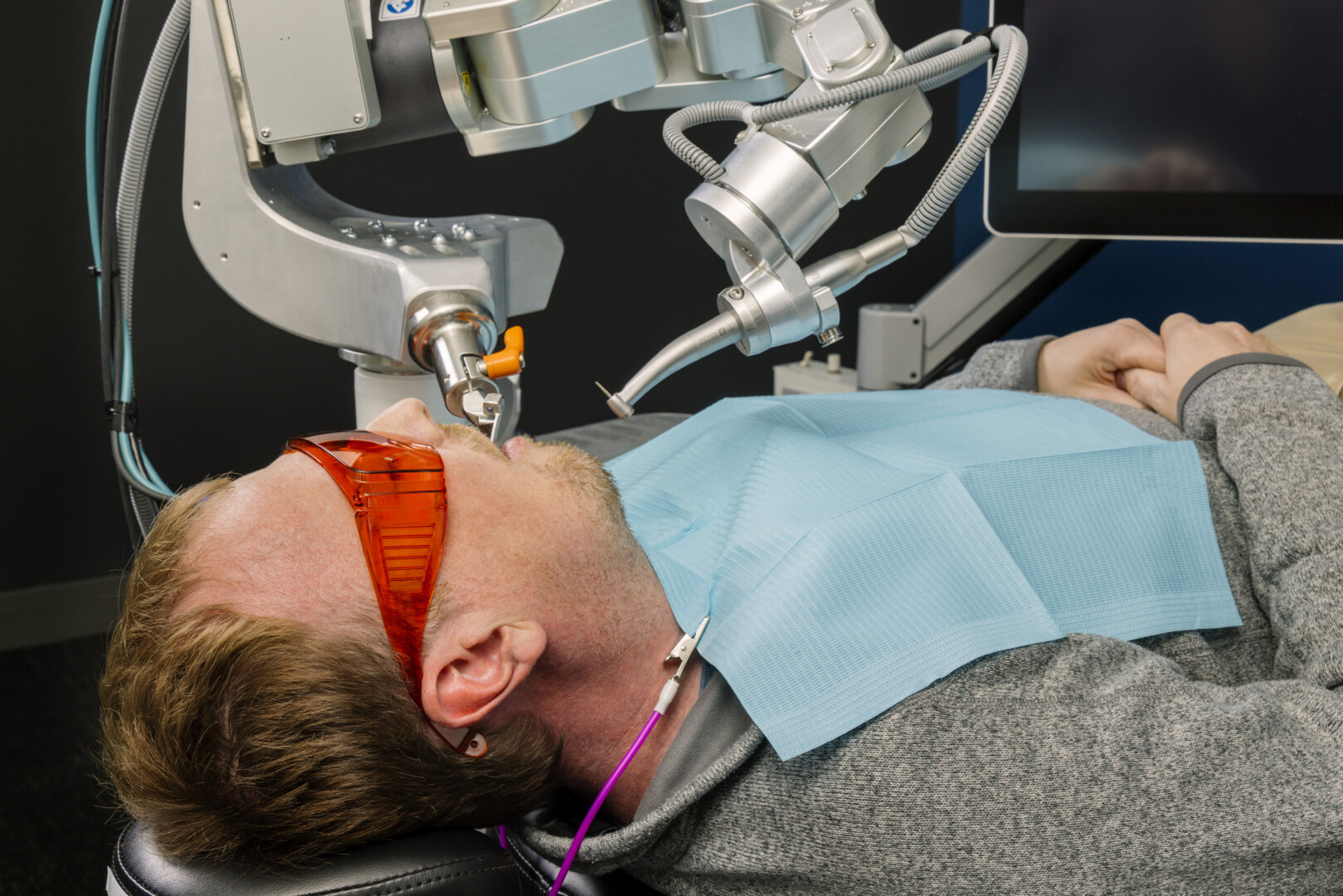 An AI-operated drill does a procedure in a patient's mouth. The patient wears orange safety glasses and a blue bib.