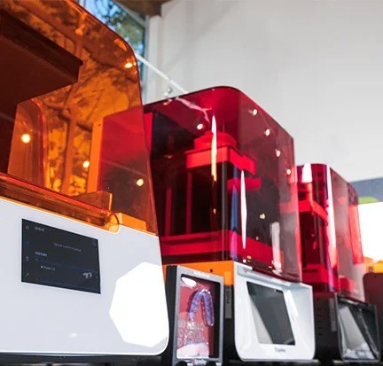 A row of 3D printers with orange plastic exteriors.