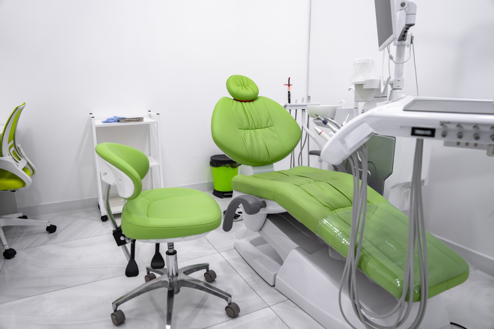 An office chair on wheels next to a dental chair for patients, both bright green.